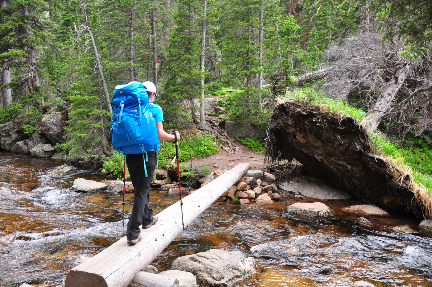 Backpacker using a log to cross a stream